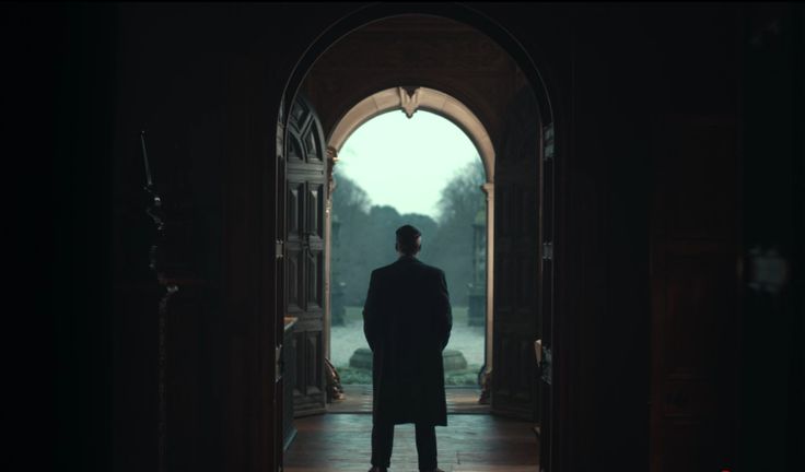 An screenshot of the show Peaky Blinders, as Thomas Shelby stands as a sillohuette in a dark hallway